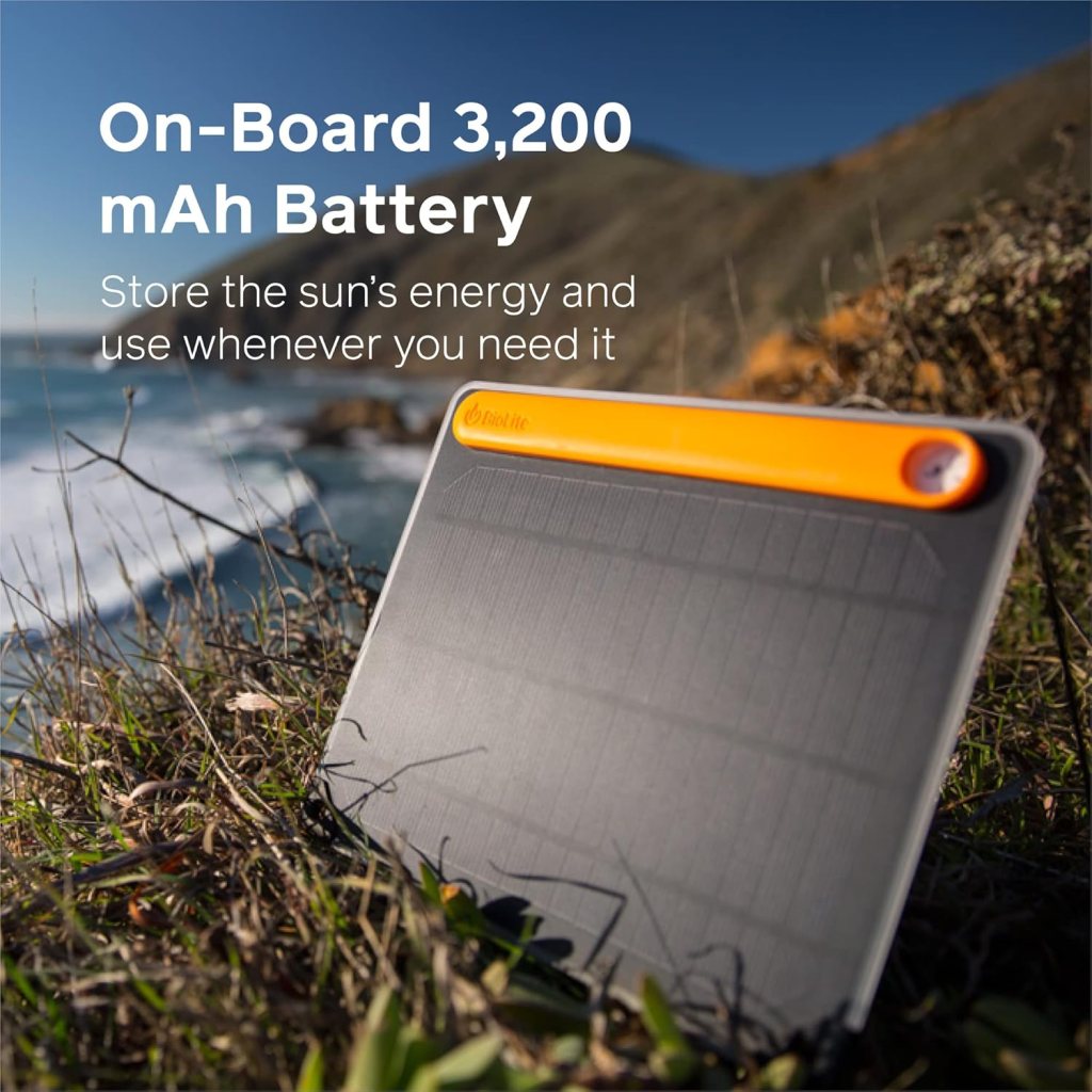 A portable solar panel with an orange stripe sits on grass overlooking a coastal cliff and ocean, showcasing its onboard 3,200 mAh battery—one of the best solar gadgets for off-grid camping 2025.